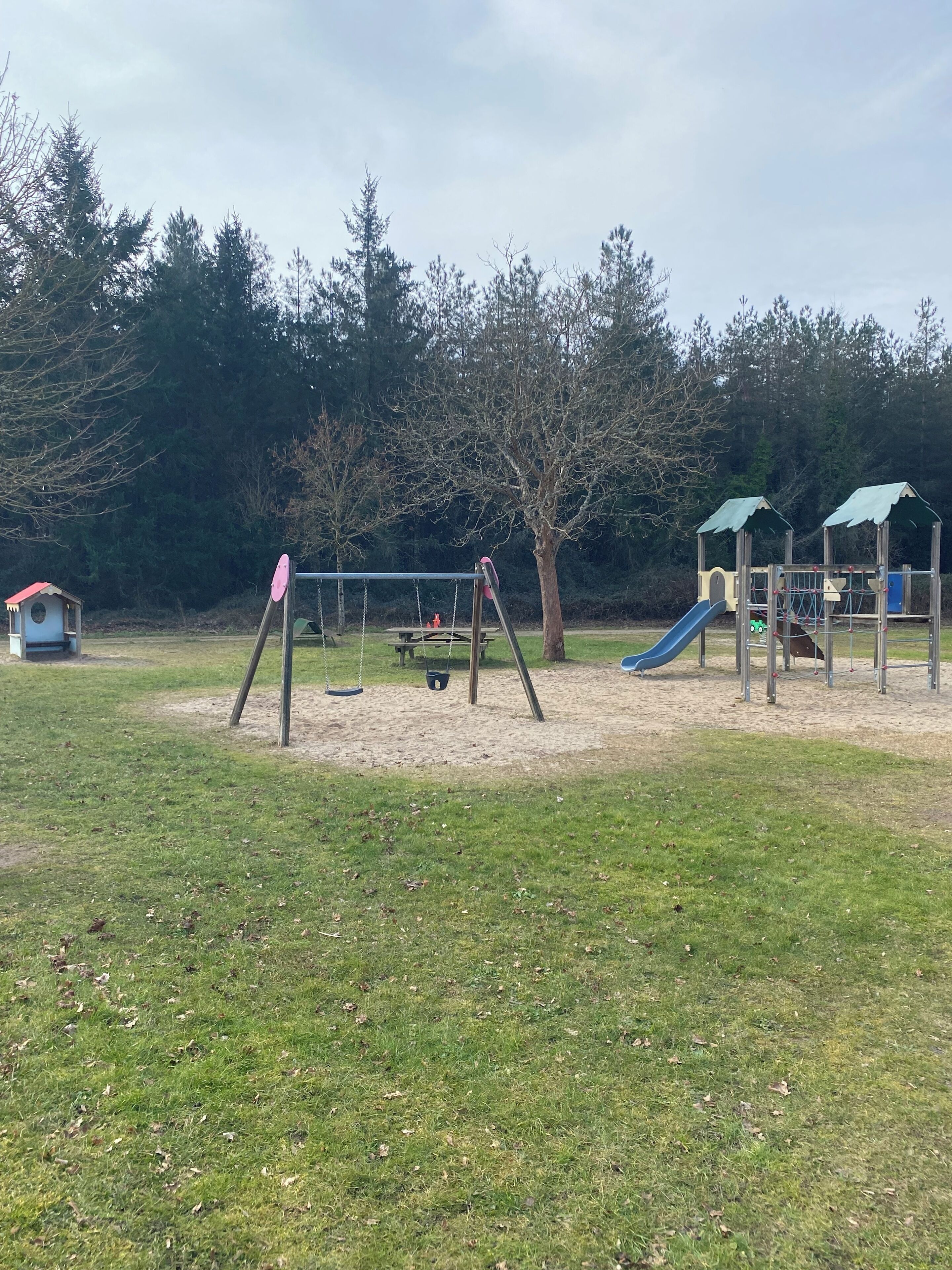 A playground with swings, a slide, and a small building.