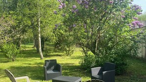 An outdoor seating area with two chairs and a table, surrounded by lush greenery and flowering trees.