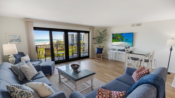 Un salon moderne avec balcon donnant sur une plage, aménagé avec un canapé, une table basse et un téléviseur.