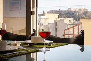 Una mesa de comedor con una copa de vino tinto, una vela y un plato de comida, con vistas a un paisaje urbano con arquitectura antigua.
