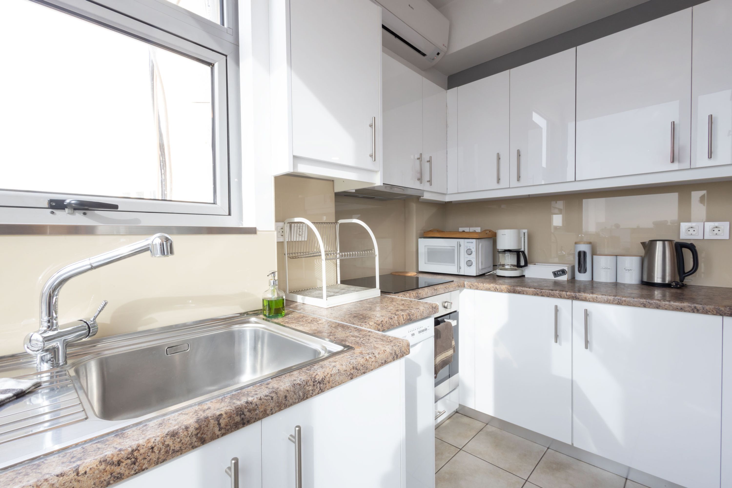 A modern kitchen with white cabinets, a granite countertop, stainless steel sink, and a window.