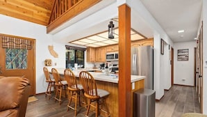 A modern kitchen with wooden cabinets, a stainless steel refrigerator, and a central island with bar stools.