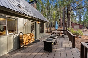 A wooden deck with outdoor seating and a stack of firewood. - Kokanee Hideaway | 5BR w/ Epic Game Room (Shaver Lake)