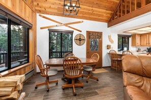 A wooden interior with a dining table, chairs, a clock, and a view of the outdoors. - Kokanee Hideaway | 5BR w/ Epic Game Room (Shaver Lake)