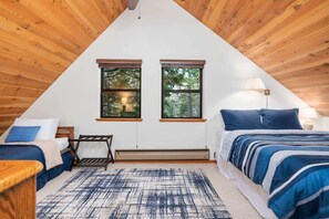 A triangular attic bedroom with two beds, a heater, and large windows with a view of trees. - Kokanee Hideaway | 5BR w/ Epic Game Room (Shaver Lake)