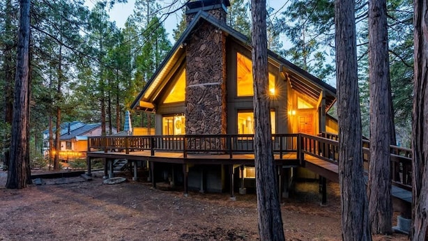 A log cabin with a stone chimney, wooden deck, and large windows.