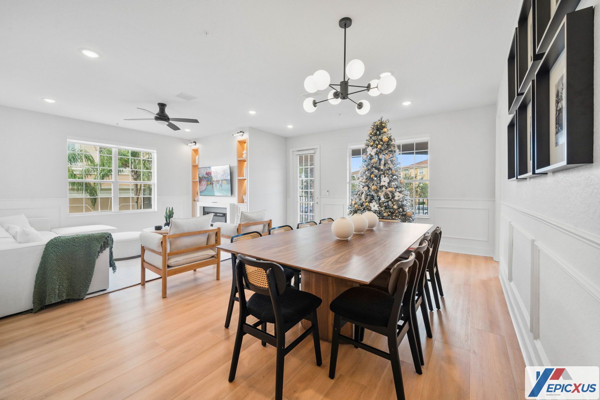 A modern living room with a wooden dining table, black chairs, a white sofa, and a large Christmas tree.