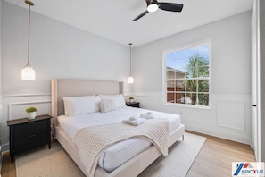 Ein Schlafzimmer mit Bett, Nachttischen, Deckenventilator und Fenster mit Blick auf Palmen.