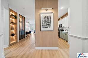 Ein modernes Interieur mit einer Wand in Holzoptik, einem gerahmten Schwarz-Weiß-Foto und einer Küchenzeile mit weißen Schränken und Geräten.