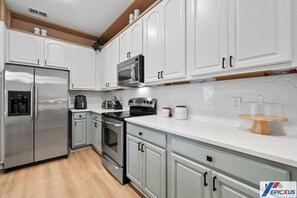 Cozinha moderna com armários brancos, eletrodomésticos de aço inoxidável e bancada de mármore.