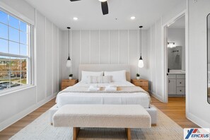 Ein modernes Schlafzimmer mit einem großen Bett, Nachttischen, einer Bank und Blick ins Freie.
