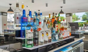 A bar with various bottles of alcohol, including Bacardi and Captain Morgan, and a laptop on the counter.