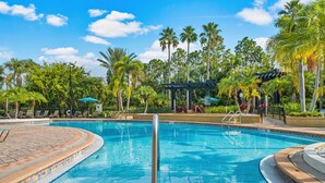 A swimming pool with a tiled deck, palm trees, lounge chairs, and a pergola.
