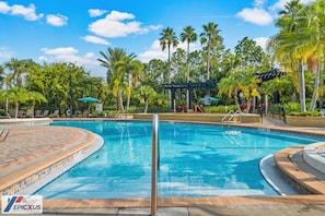 Ein Pool mit gefliestem Sonnendeck, Palmen, Liegestühlen und einer Pergola.