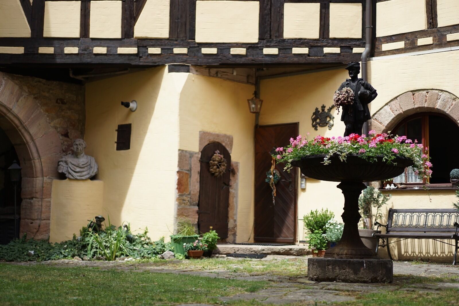 A courtyard with a fountain, a statue, and a building with a timber-framed facade.