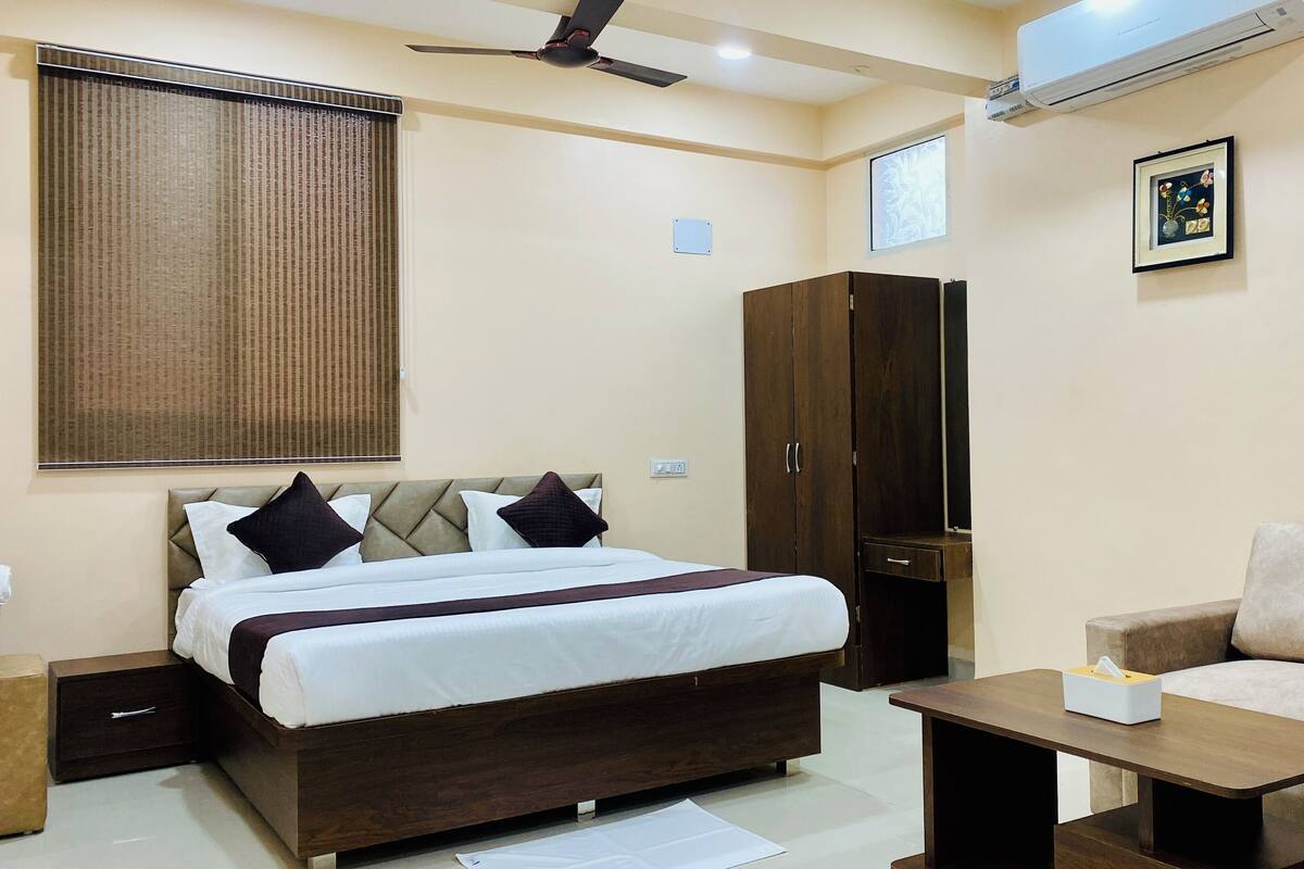 A hotel room with a bed, a wardrobe, a sofa, a bedside table, and a ceiling fan.