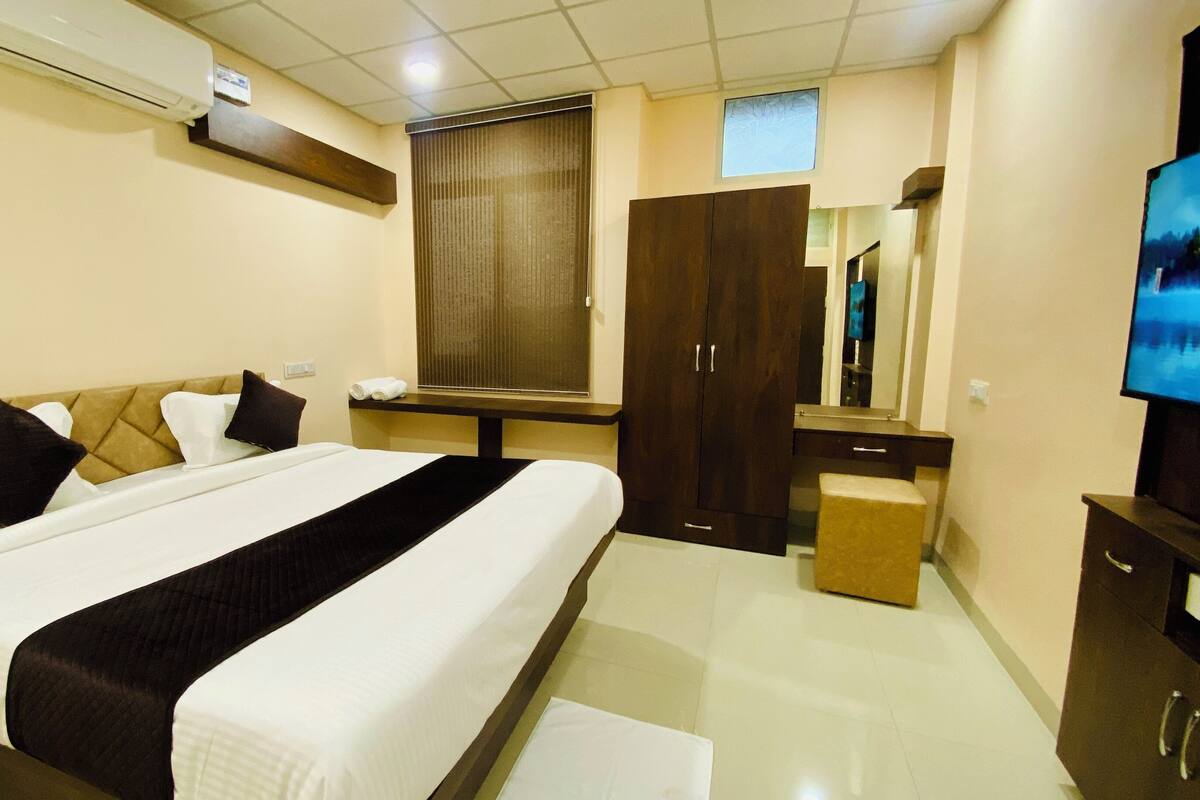 A hotel room with a large bed, a desk, a mirror, and a TV.