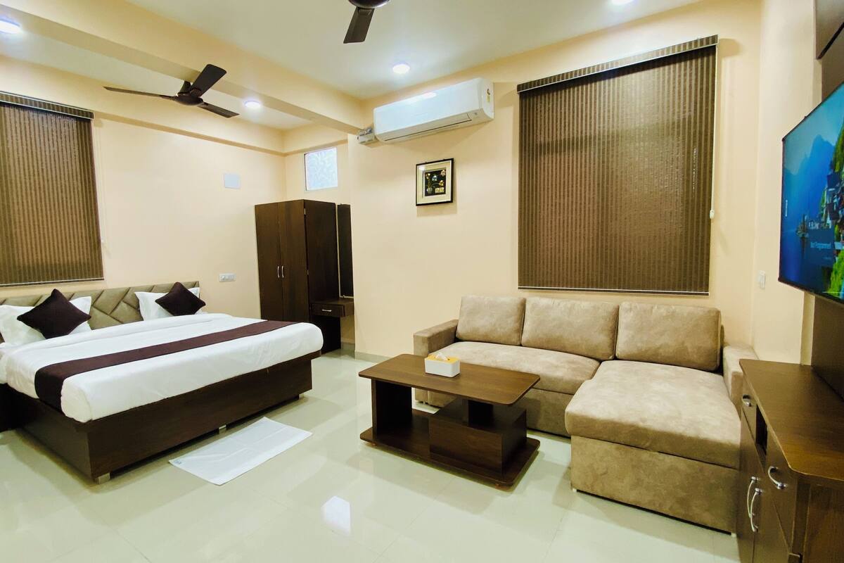 A modern hotel room with a large bed, a sofa, a coffee table, and a TV.
