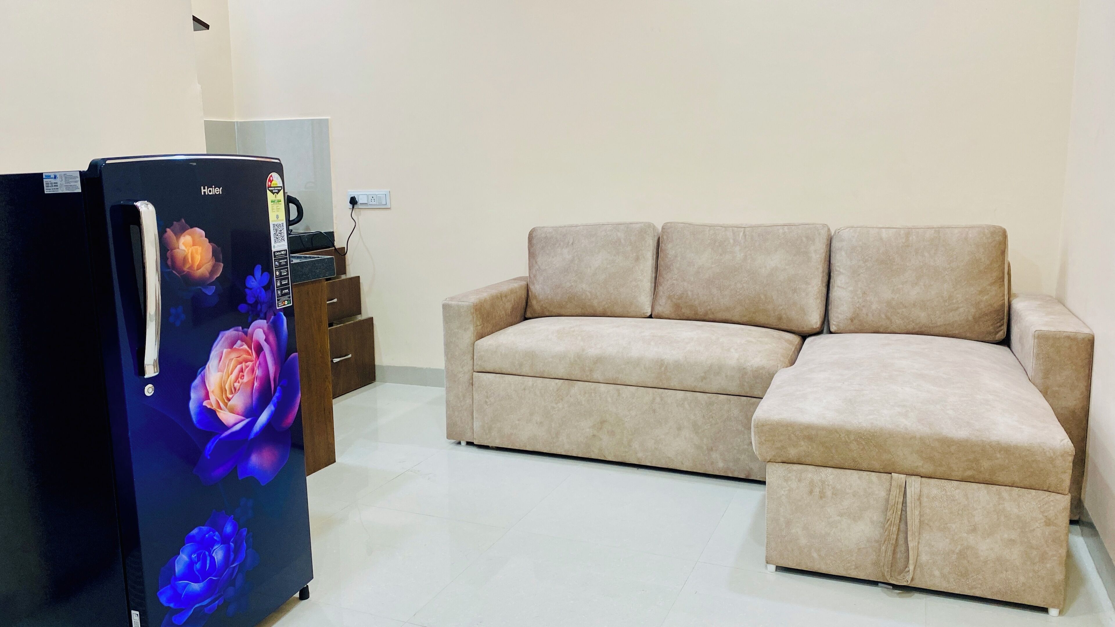 A living room with a beige sofa, a black refrigerator with a floral display, and a small wooden side table.