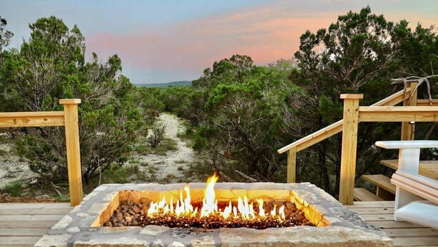 A stone fire pit on a wooden deck with a view of a forested area.