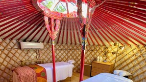 A cozy interior of a traditional yurt with two beds, a small table, and a hanging light fixture.