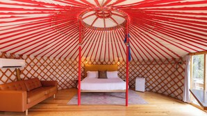 A yurt with a central bed, a sofa, and a window.