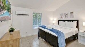 Une chambre à coucher comprenant un lit, des tables de chevet, une fenêtre, un climatiseur et un téléviseur fixé au mur.