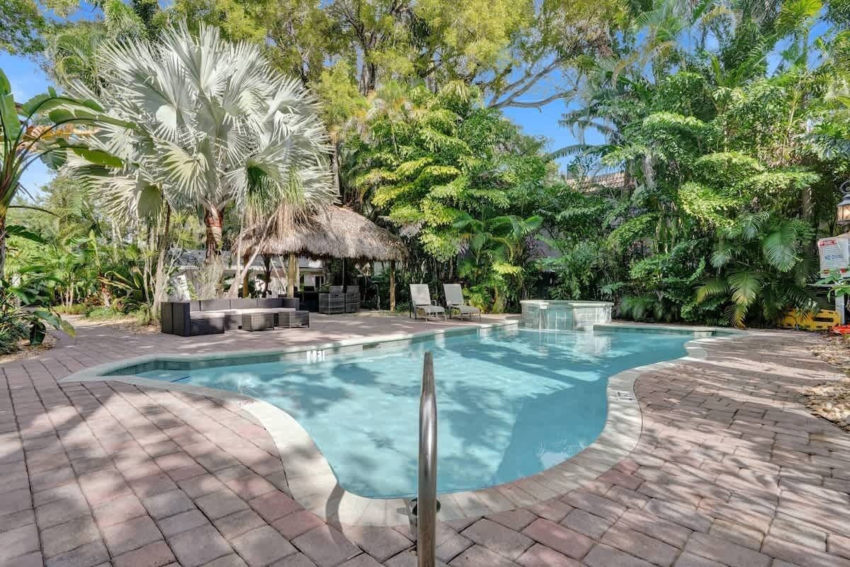 Pool deck with thatched-roof cabana, lounge chairs, and mature palms creating shaded tropical setting