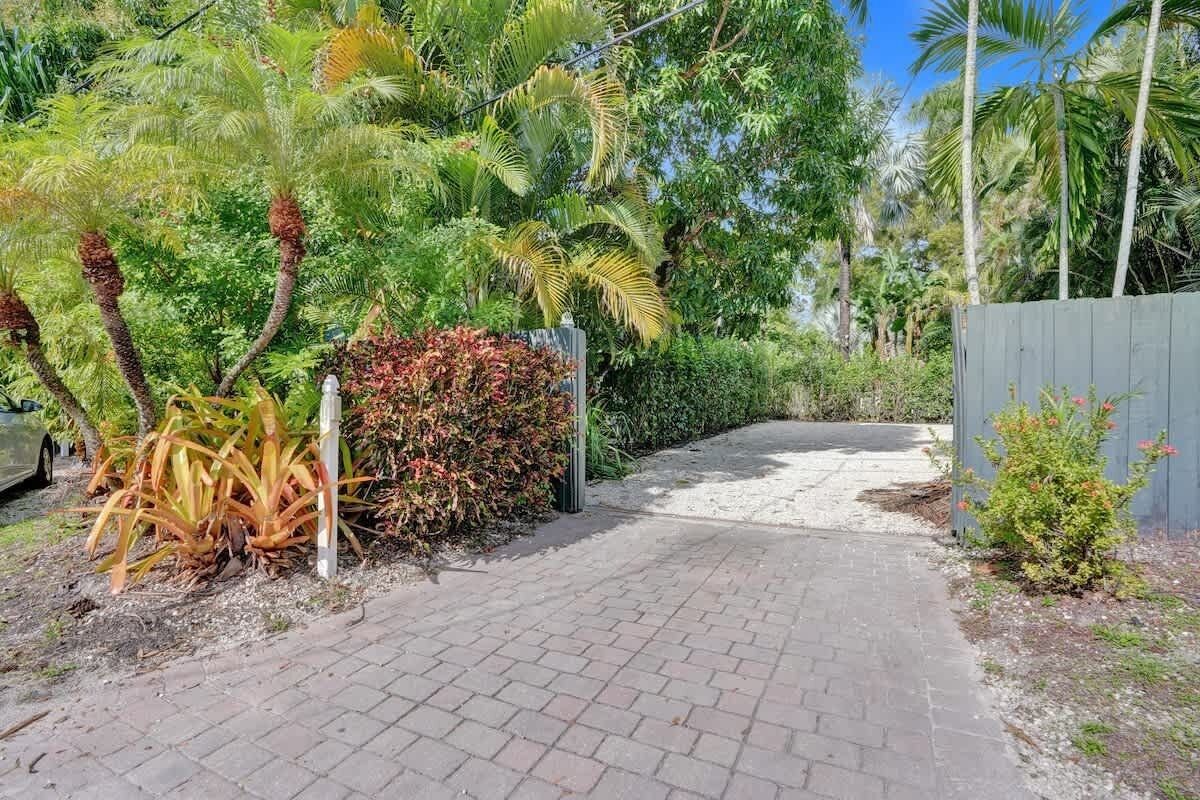 A paved pathway leading through a lush garden with various tropical plants and a wooden fence.