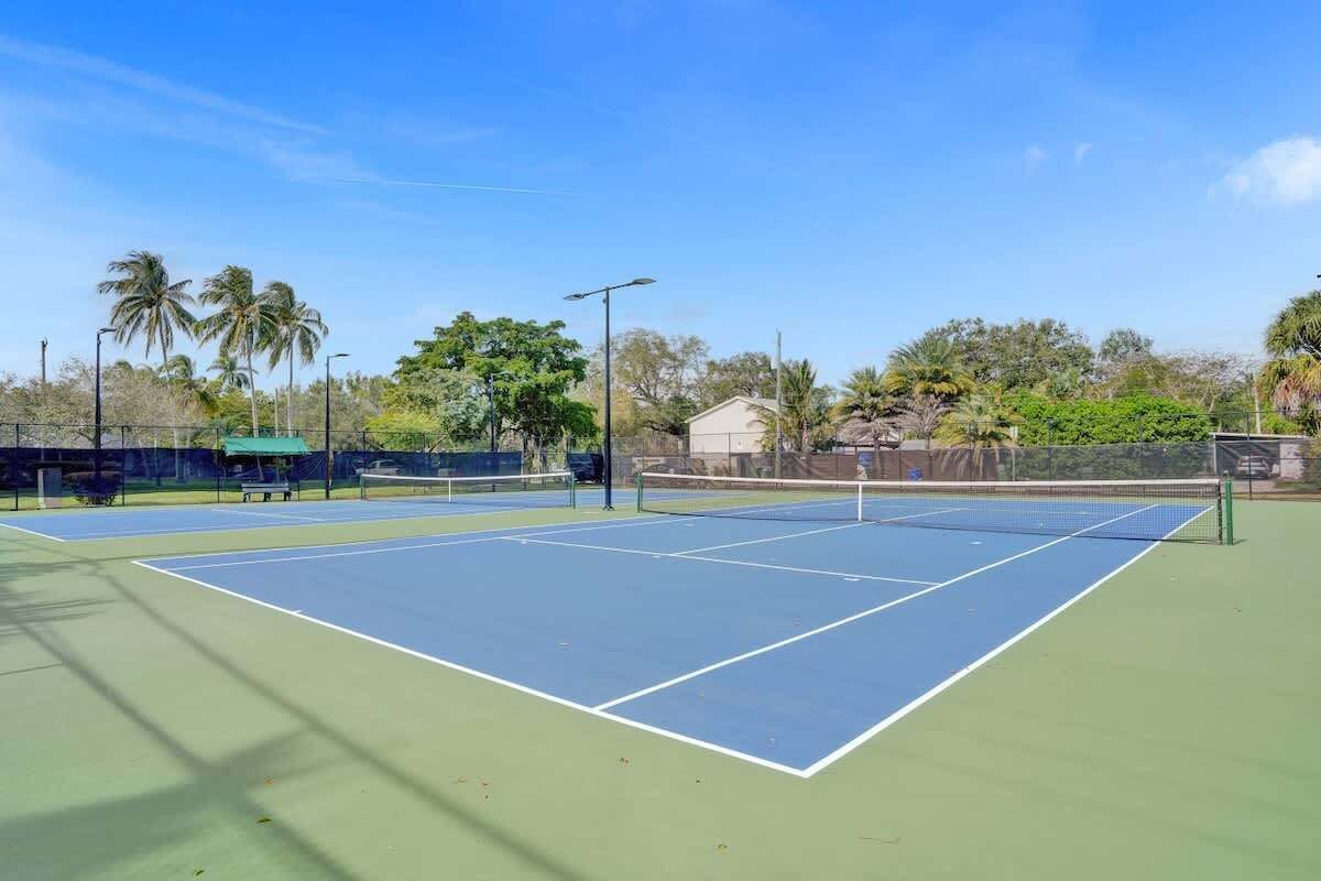 Een tennisbaan met een net, omringd door groen en een gebouw op de achtergrond.