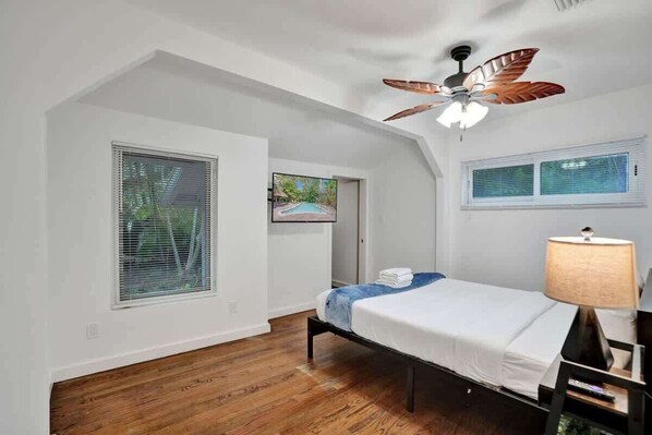 Un dormitorio con una cama, ventilador de techo y ventana con persianas.