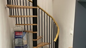 A spiral staircase with wooden steps and black railings, a metal ladder, and a Viledia Universal package in the background. - Getaway to Carmaux (Carmaux)