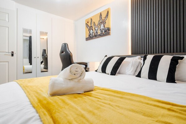 A hotel room with a bed, a painting of donkeys, a chair, and a desk.