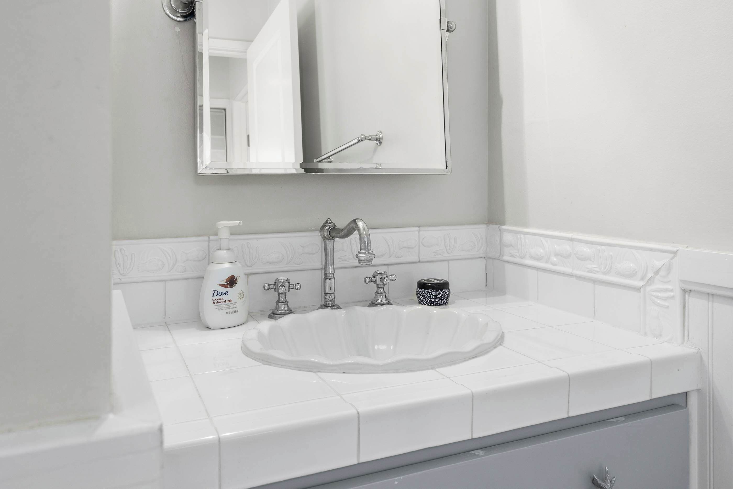 A bathroom with a white sink, a mirror, and a Dove hand soap dispenser.
