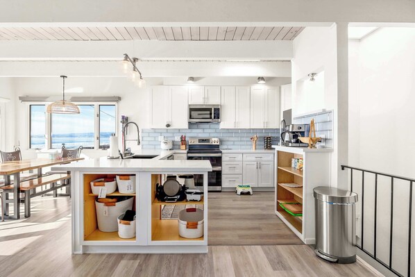 Une cuisine moderne avec des meubles blancs, un îlot central doté de rangements, un four à micro-ondes, une cuisinière et une vue sur l’extérieur.