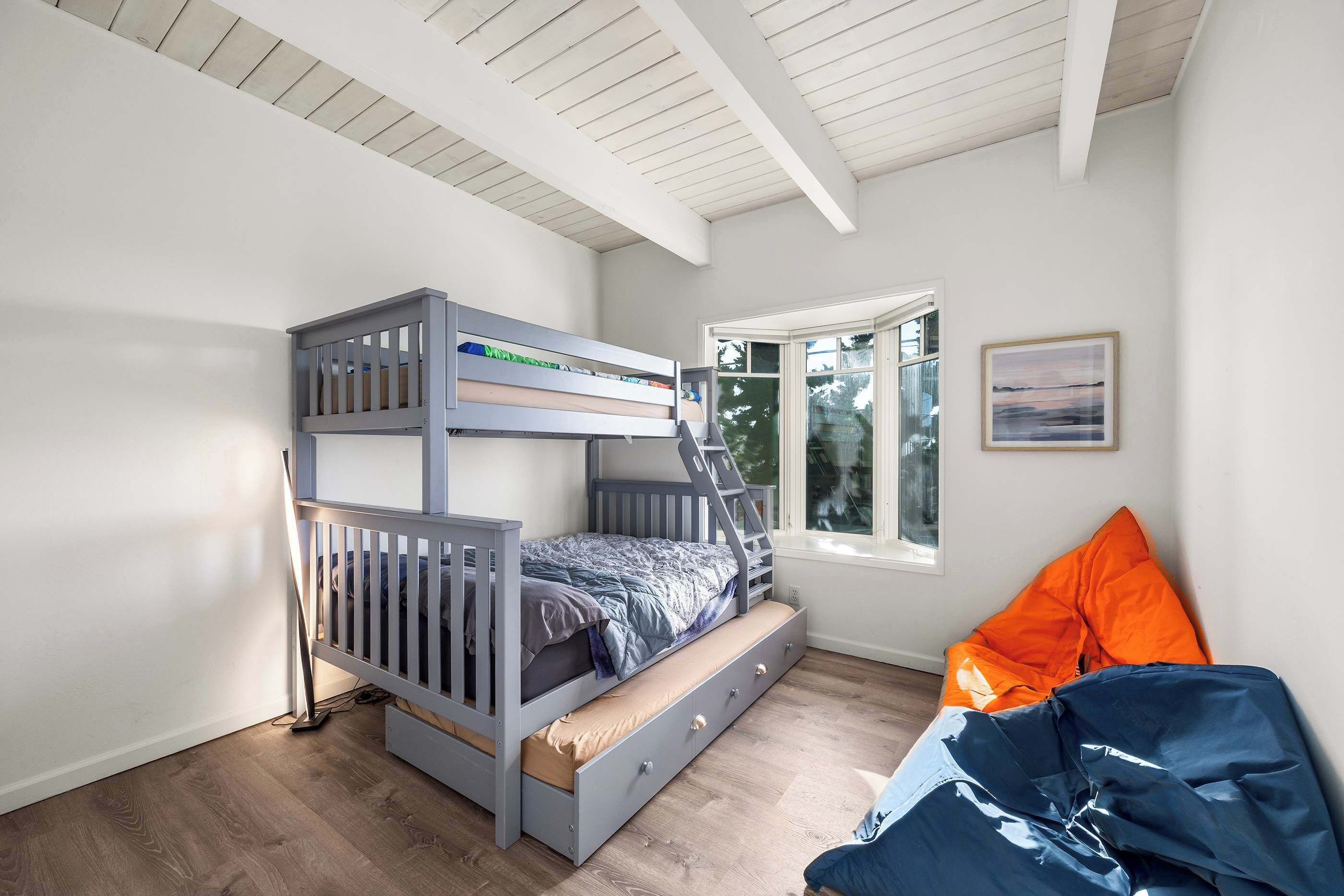 Un lit superposé avec une échelle, une fenêtre donnant sur un beau paysage et un lit avec des oreillers orange.