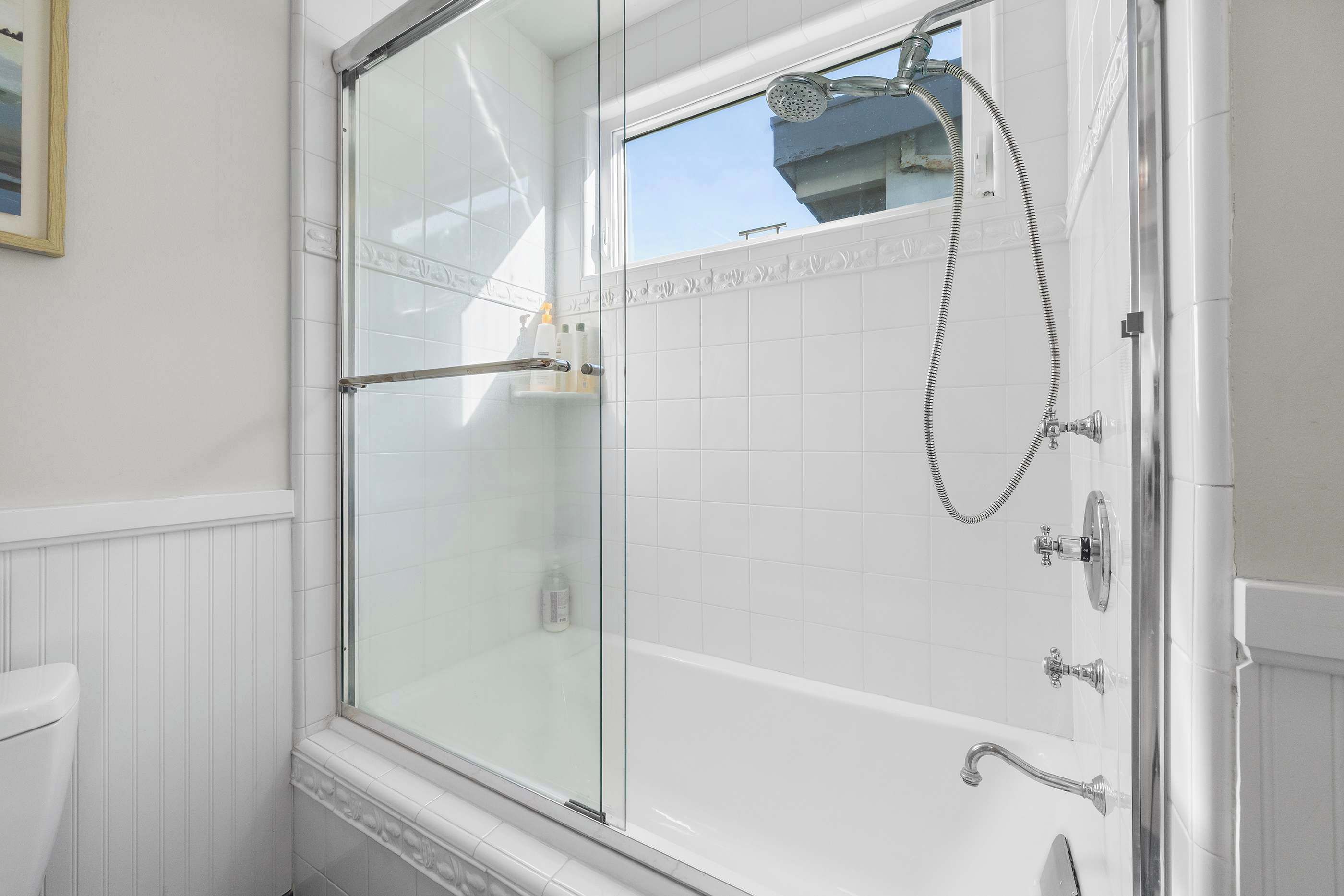 A glass-enclosed shower with a handheld showerhead, a glass door, and a window above the shower.