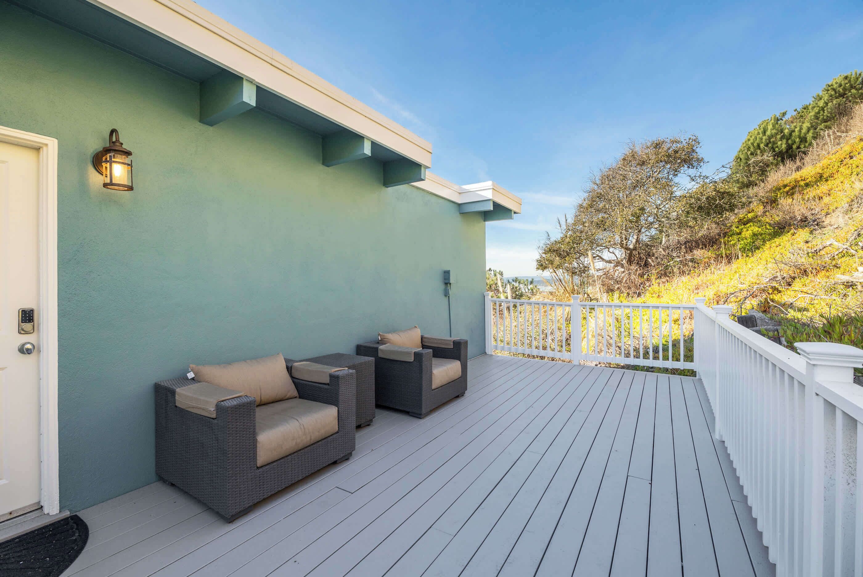 A covered outdoor area with a light-colored deck, a white railing, and two wicker sofas with cushions.