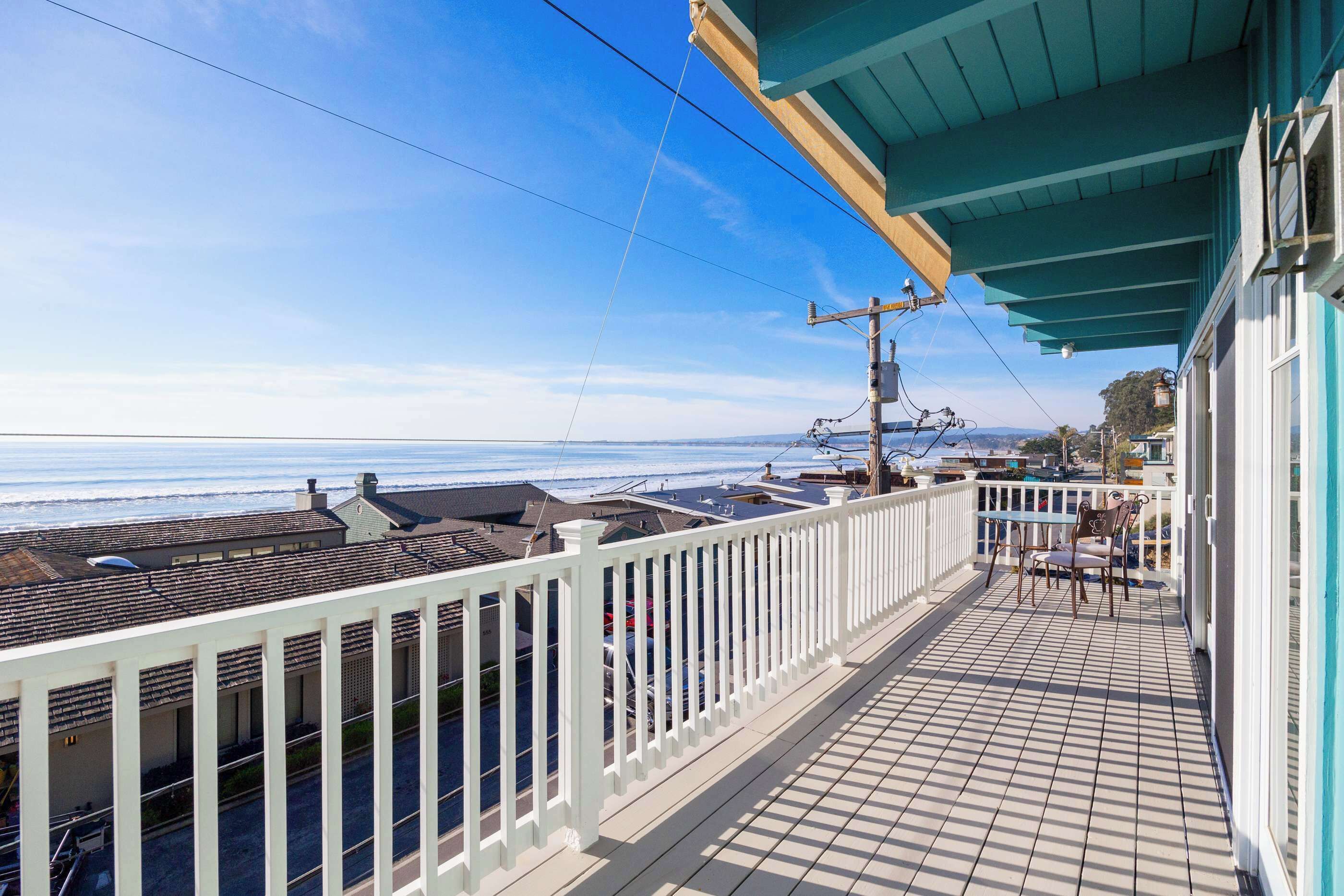 A balcony with a view of the ocean, a white railing, and a table with chairs.