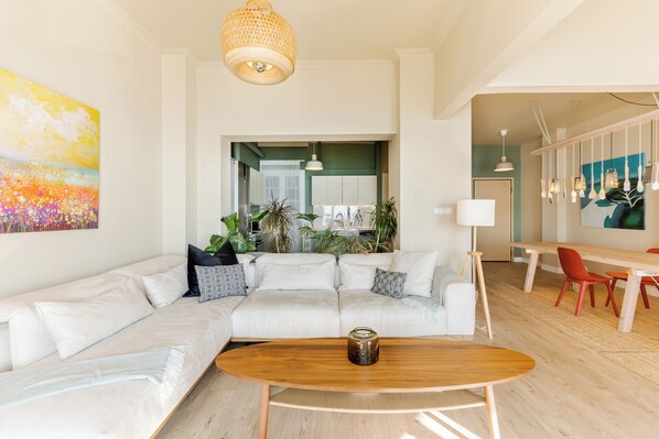 A modern living room with a sectional sofa, a wooden coffee table, and a dining area with red chairs. - Infinity & Beyond Seafront Apartments by Halu! (Thessaloniki)
