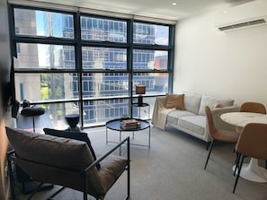 Ein modernes Wohnzimmer mit großem Fenster, einer Couch, einem Couchtisch und einem Essbereich.
