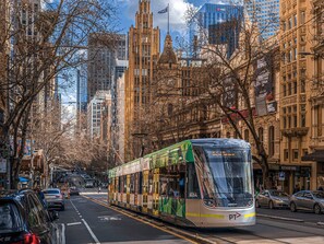 A tram with a green and white design, a clear view of the street, and tall buildings in the background.
