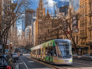 A tram with a green and white design, a clear view of the street, and tall buildings in the background.