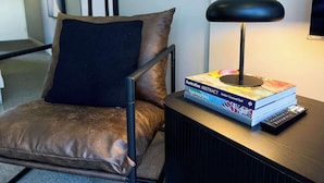 A chair with a brown cushion, a black lamp, and a stack of books on a table. - Modern and Elegant 1BD Apartment in the CBD (Melbourne)
