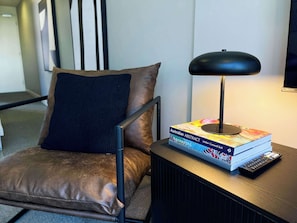 Ein Stuhl mit brauner Sitzkissen, eine schwarze Lampe und ein Bücherstapel auf einem Tisch.