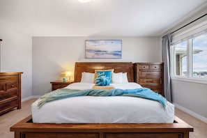 Uma cama bem arrumada com travesseiro azul, cabeceira de madeira, mesa de cabeceira com abajur e janela com cortinas.