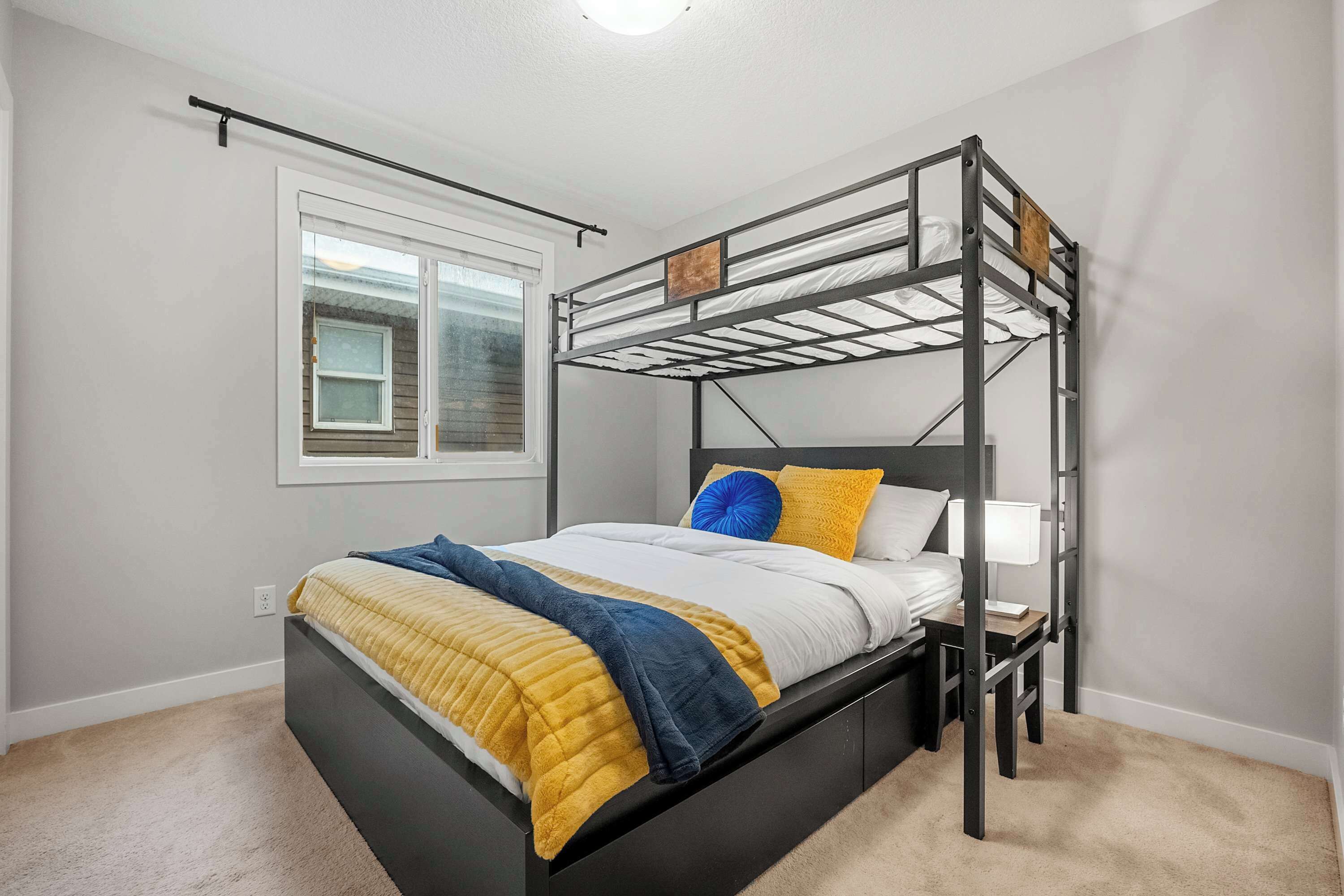 A bunk bed with a headboard, a bedside table, and a window with blinds.