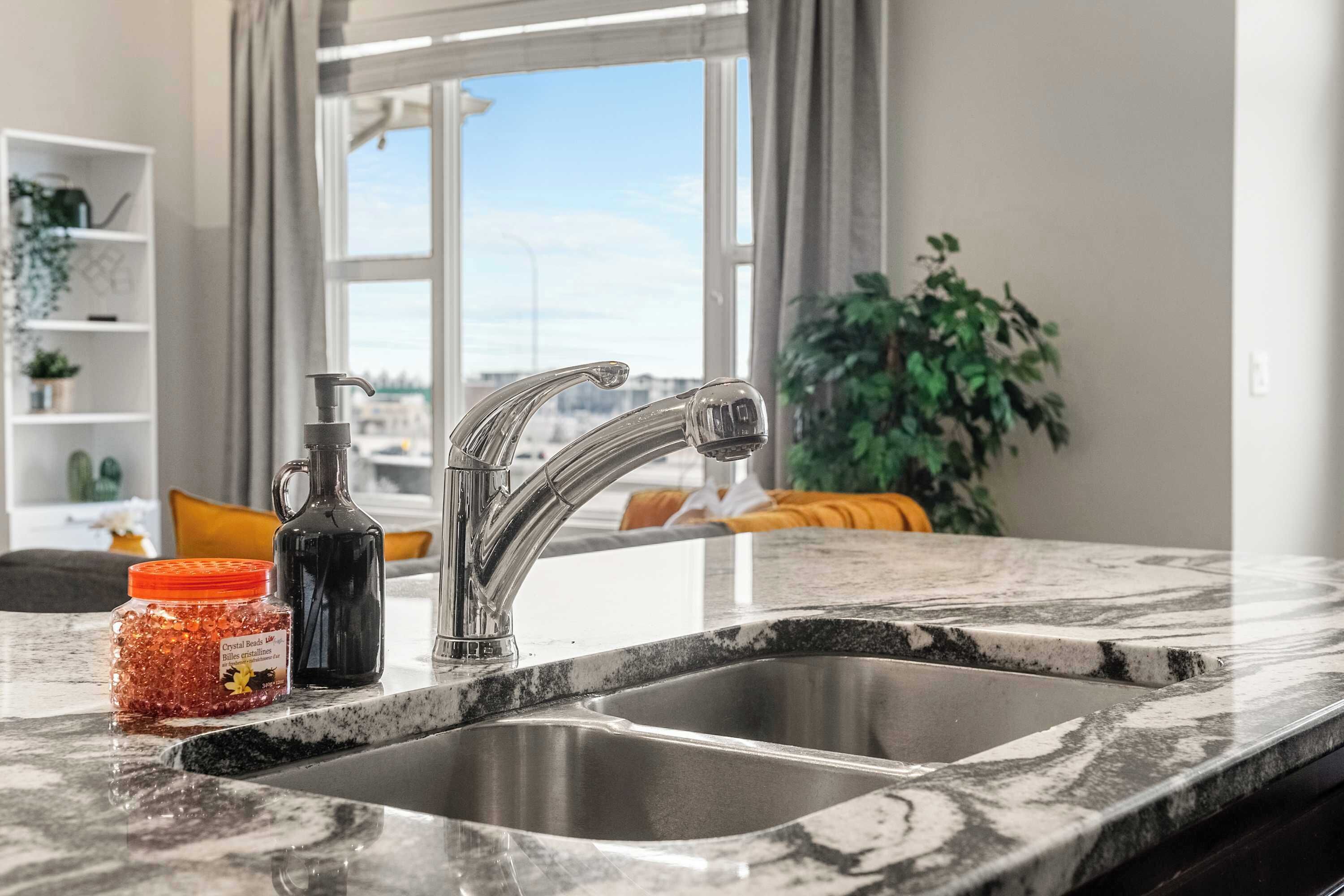 A kitchen with a double sink, a marble countertop, a bottle of honey, and a pitcher.
