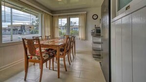 A dining area with a wooden table and chairs, large windows with curtains, a clock on the wall, and a kitchen area with a refrigerator. - LOOK!  Spacious Home in the Heart of Hilo - Bonus Rec Room! (Hilo)