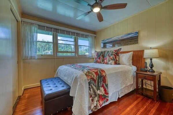 A bedroom with a bed, a ceiling fan, a nightstand, and a window with curtains.